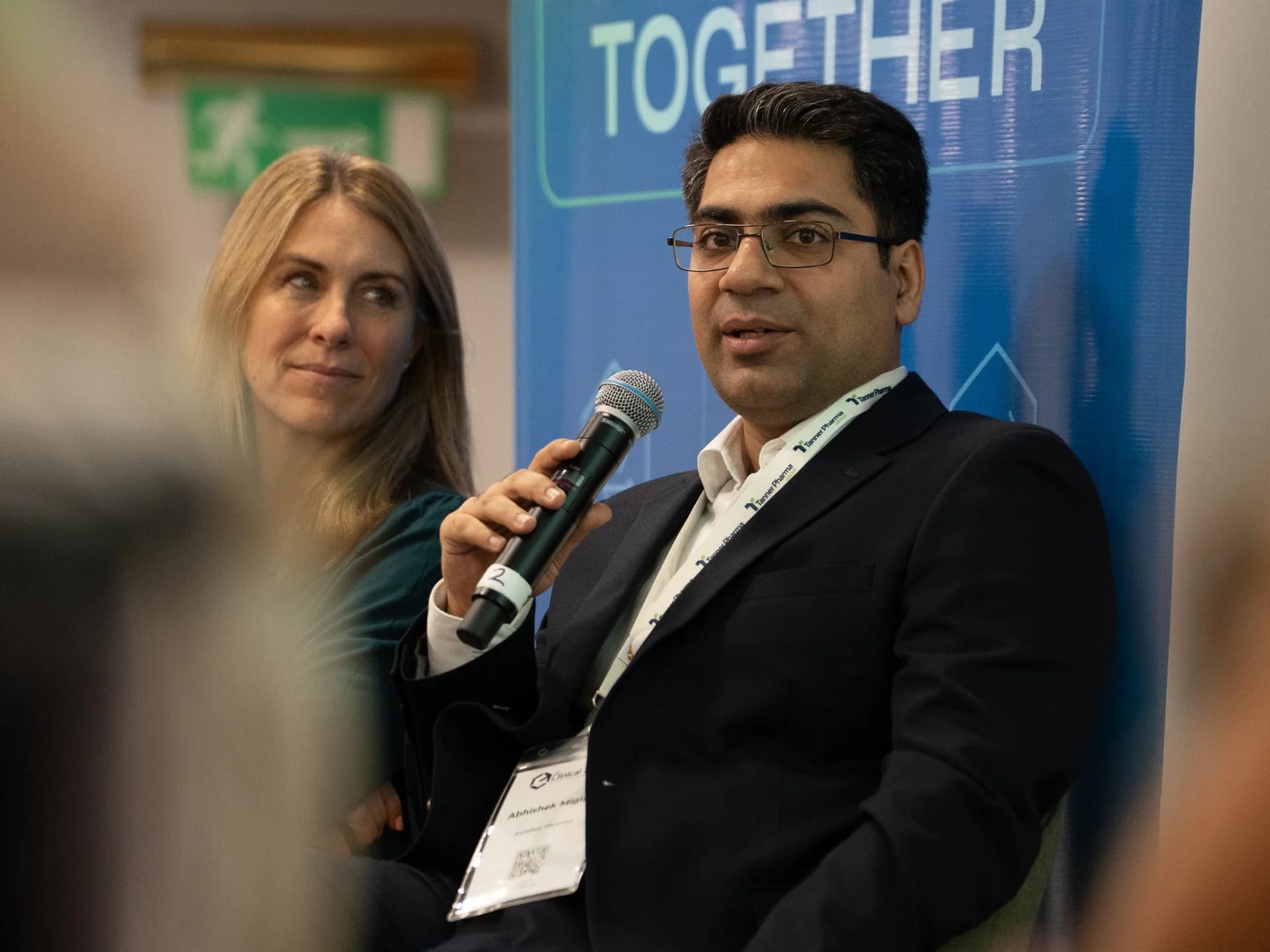 A panellist speaking into a microphone, with a colleague looking on